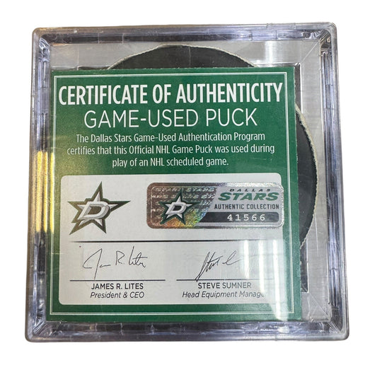A game-used hockey puck in a clear plastic protective case with a green and white Certificate of Authenticity insert. 
COA 
