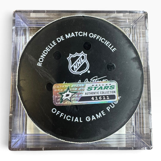 An official Dallas Stars hockey puck displayed inside a clear acrylic case. The black puck features white text reading &