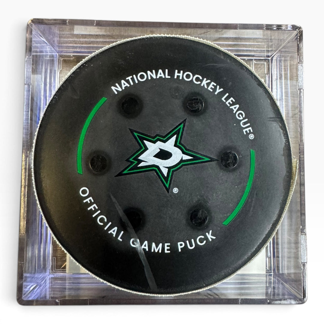 A black Dallas Stars National Hockey League official game puck displayed inside a clear square plastic case on a white background.