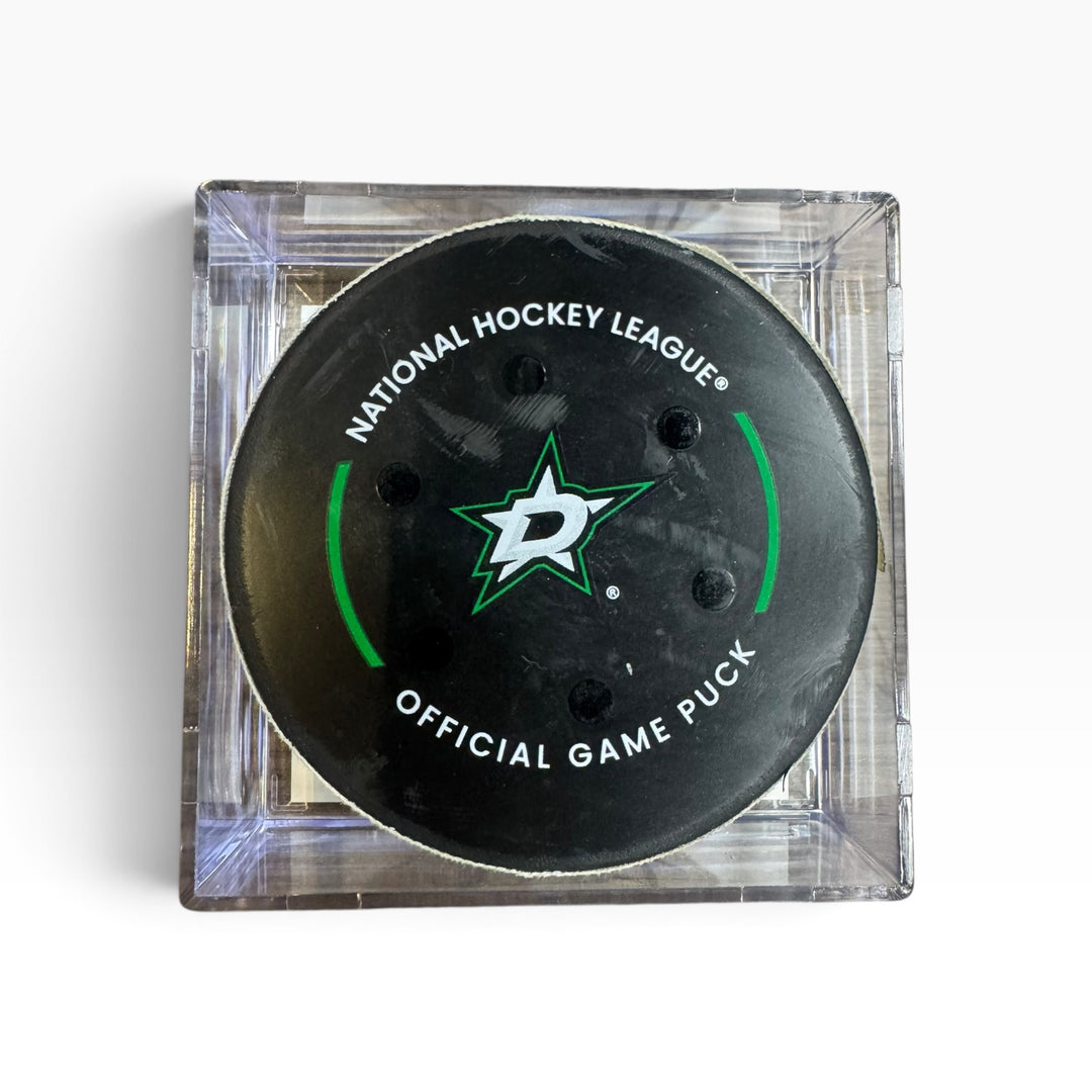 A Dallas Stars National Hockey League official game puck in a clear square plastic display case, photographed from directly above on a white background.