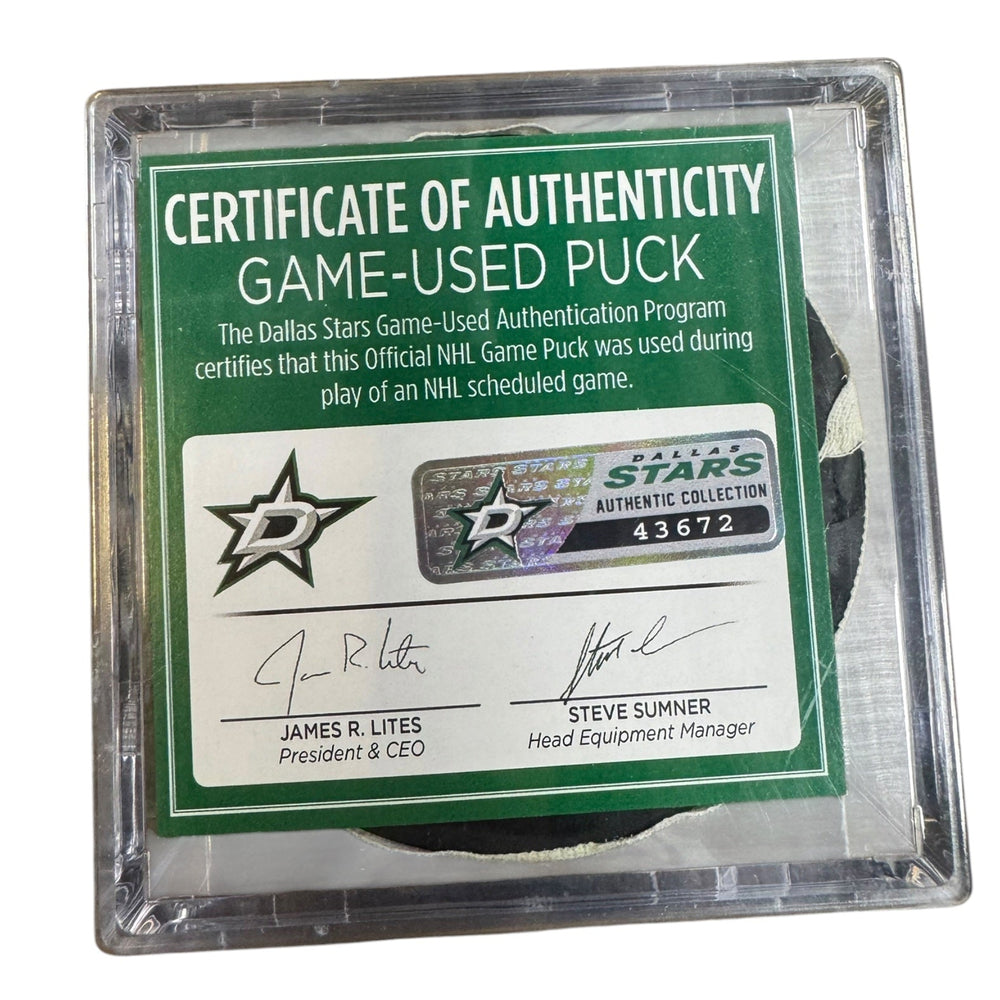 A game-used hockey puck in a clear plastic protective case with a green and white Certificate of Authenticity insert. 
COA #43672