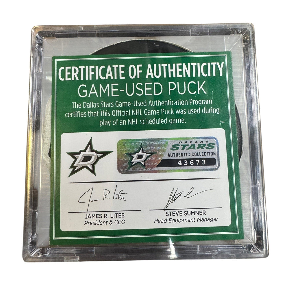 A game-used hockey puck in a clear plastic protective case with a green and white Certificate of Authenticity insert. 
COA #43673
