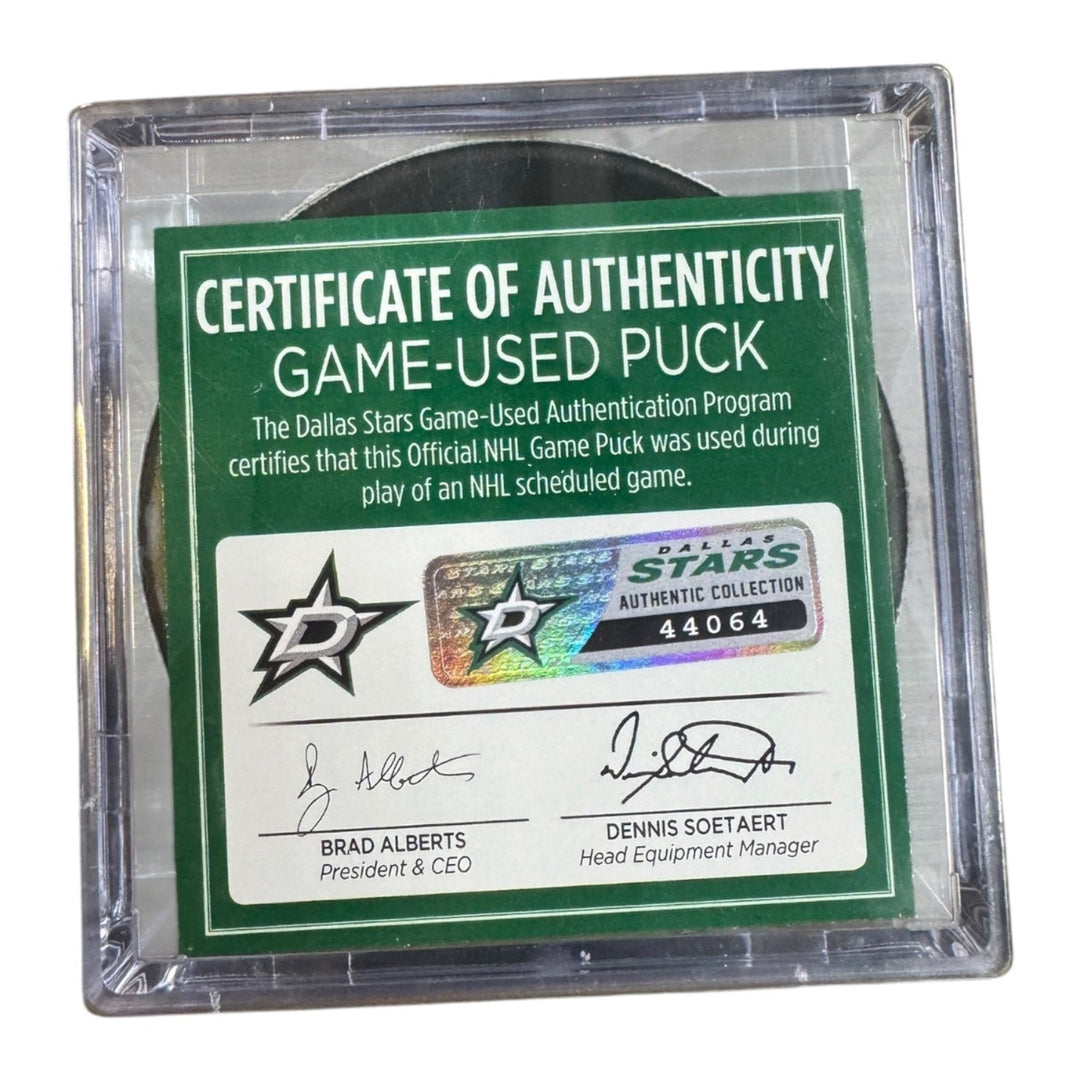 A game-used hockey puck in a clear plastic protective case with a green and white Certificate of Authenticity insert. COA 