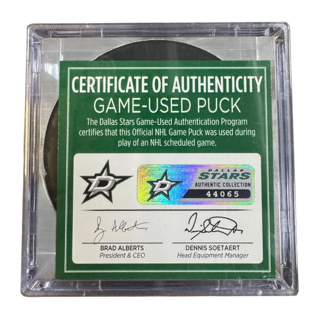 A game-used hockey puck in a clear plastic protective case with a green and white Certificate of Authenticity insert. COA 