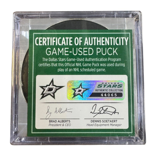 A game-used hockey puck in a clear plastic protective case with a green and white Certificate of Authenticity insert. COA 