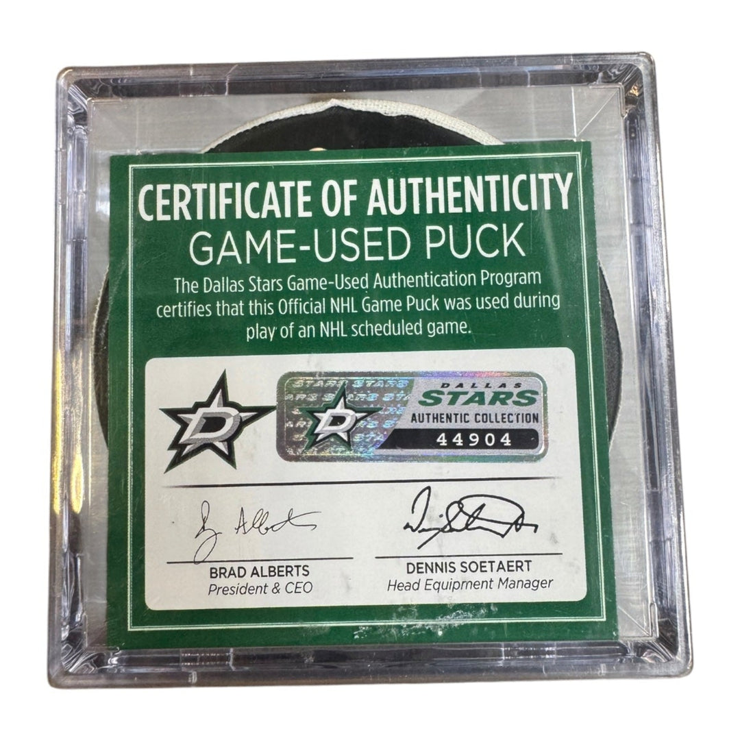 A game-used hockey puck in a clear plastic protective case with a green and white Certificate of Authenticity insert. COA 