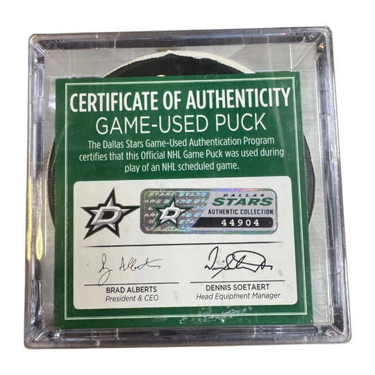 A game-used hockey puck in a clear plastic protective case with a green and white Certificate of Authenticity insert. COA 