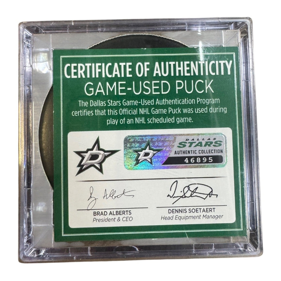 A game-used hockey puck in a clear plastic protective case with a green and white Certificate of Authenticity insert. COA 