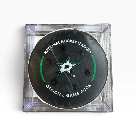A Dallas Stars National Hockey League official game puck in a clear square plastic case, photographed from above on a white background.