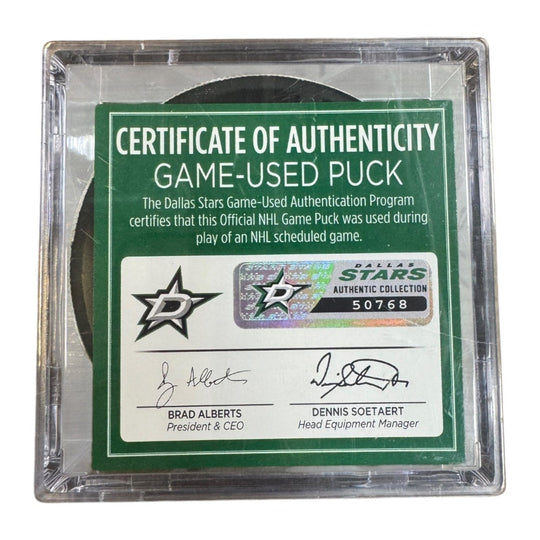 A game-used hockey puck in a clear plastic protective case with a green and white Certificate of Authenticity insert. COA 