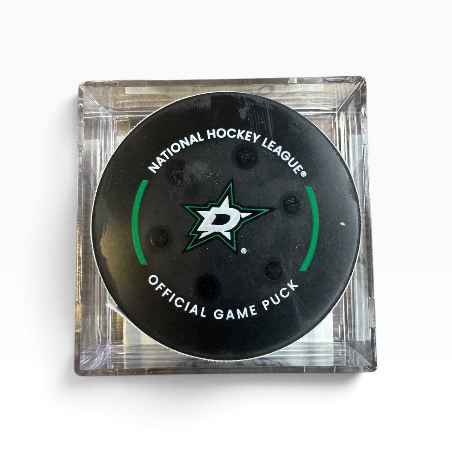 A Dallas Stars National Hockey League official game puck in a clear square plastic display case, photographed from directly above on a white background.