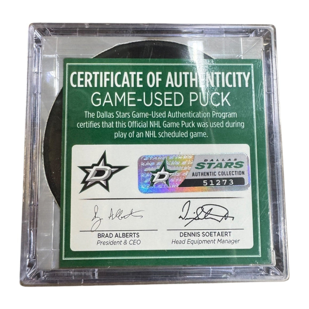 A game-used hockey puck in a clear plastic protective case with a green and white Certificate of Authenticity insert. COA 