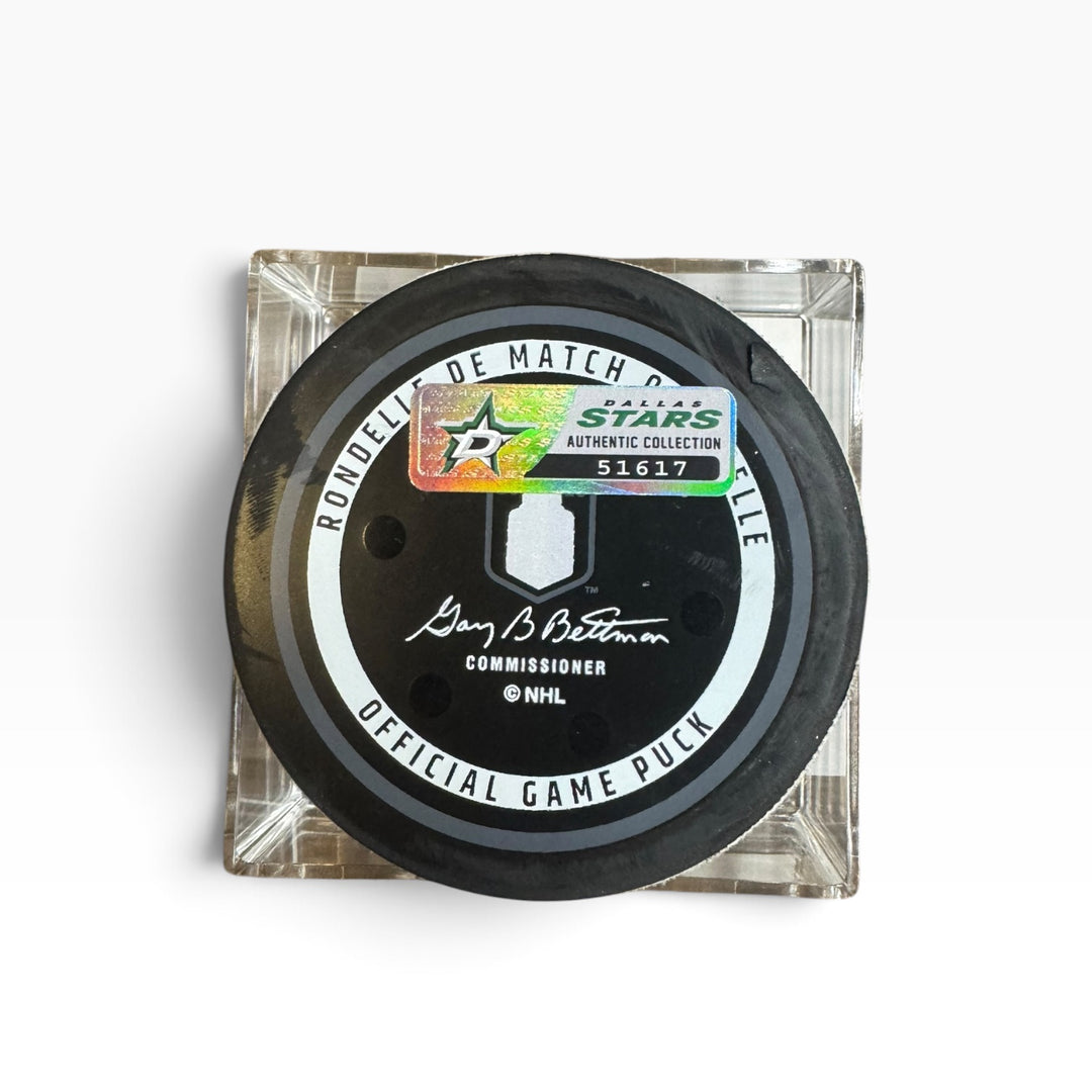 An official NHL hockey game puck displayed on a clear acrylic block against a white background. The puck features a black face with a white circular band and a holographic  authentic sticker