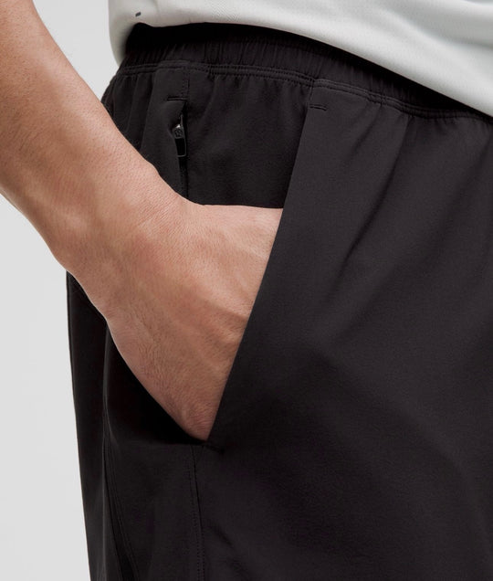 Close-up of a person wearing black athletic shorts, showing a side pocket with a zipper and the hand reaching into the pocket.