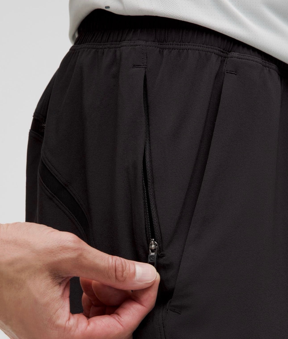 Close-up of a person wearing black athletic shorts, showing a side zip pocket being opened by a hand.