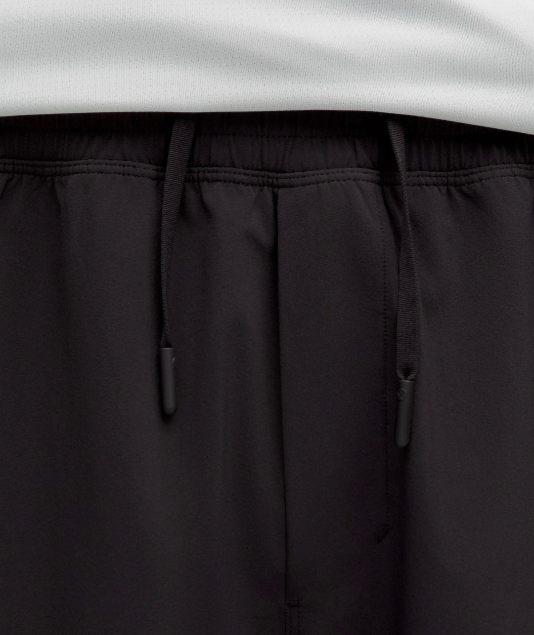 Close-up of black drawstring shorts with an elastic waistband, showing the black drawstrings and a white garment hem at the top.