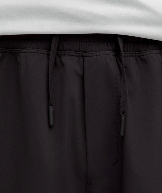 Close-up of black drawstring shorts with an elastic waistband, showing the black drawstrings and a white garment hem at the top.