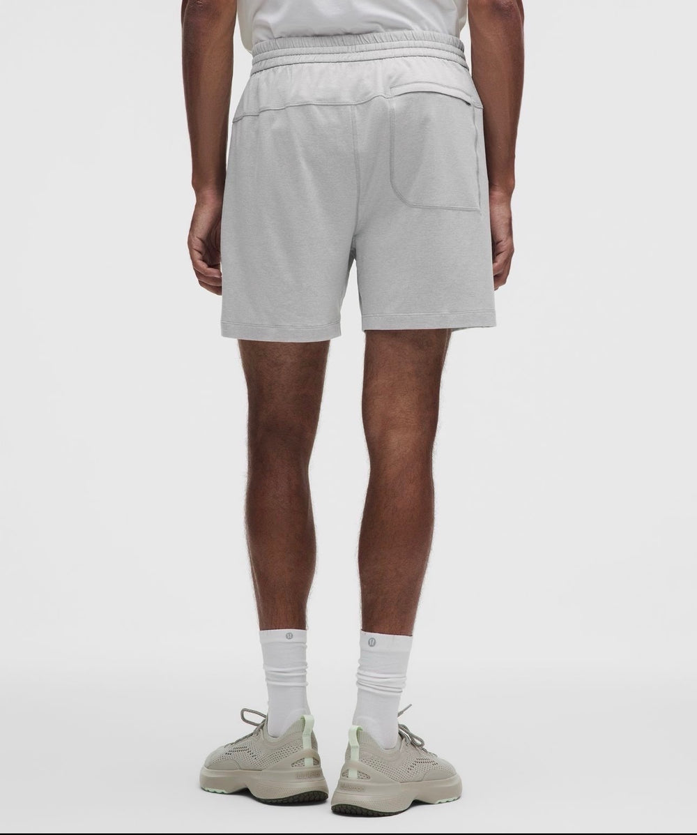 A person shown from the back wearing light gray heathered athletic shorts, white crew socks, and beige sneakers against a clean light gray studio background.