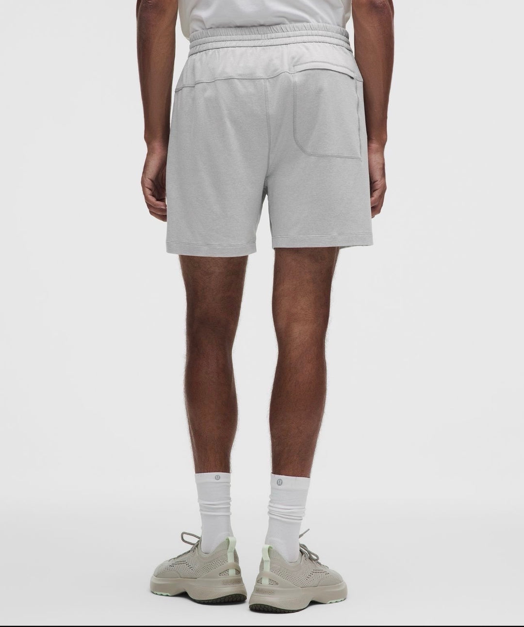 A person shown from the back wearing light gray heathered athletic shorts, white crew socks, and beige sneakers against a clean light gray studio background.