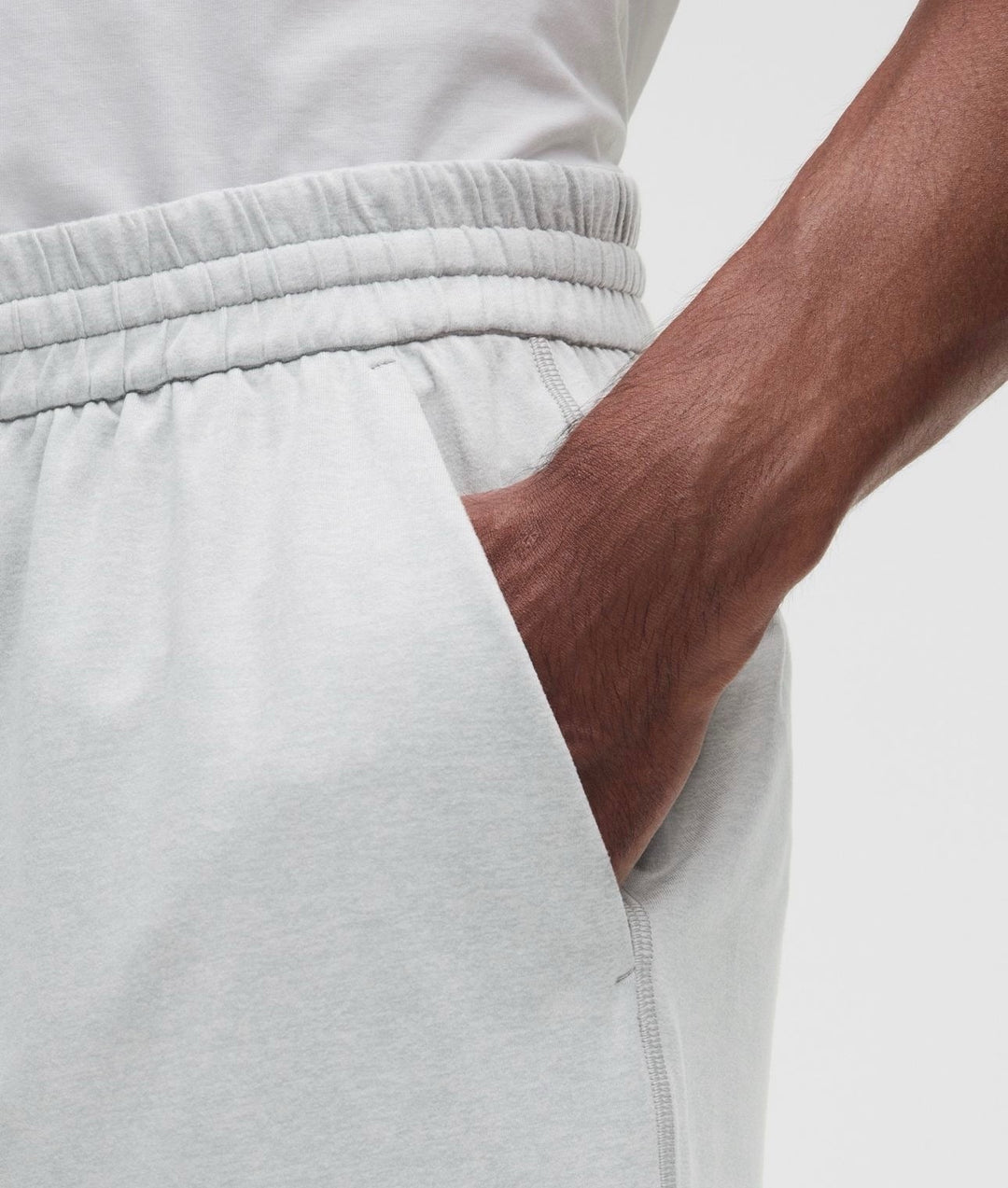 Close-up of a person wearing light gray heather Shorts, showing the side pocket with a hand inserted and the elastic waistband.