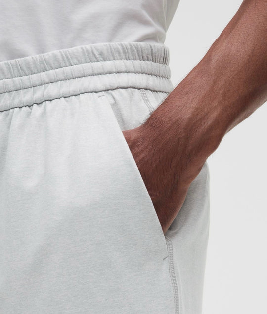Close-up of a person wearing light gray heather Shorts, showing the side pocket with a hand inserted and the elastic waistband.