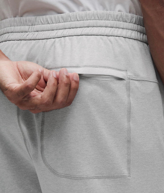Close-up of a person wearing light gray heather shorts, showing the back pocket and hand pulling the pocket flap open.