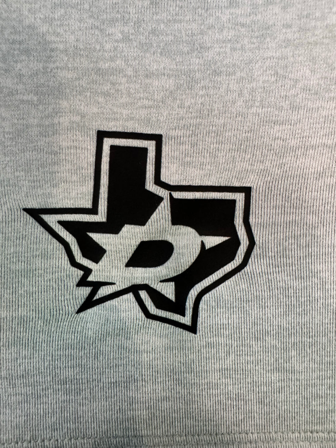 Close-up of a light heather gray fabric with a black and white stylized graphic logo printed on the front.