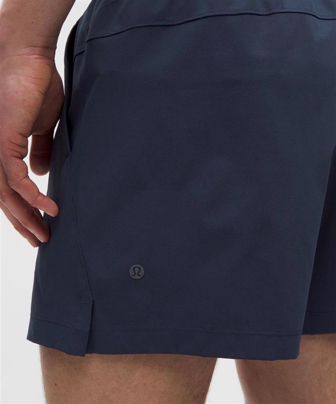 Close-up of a person wearing navy athletic shorts, showing the side pocket and a small circular Lululemon logo near the hem.