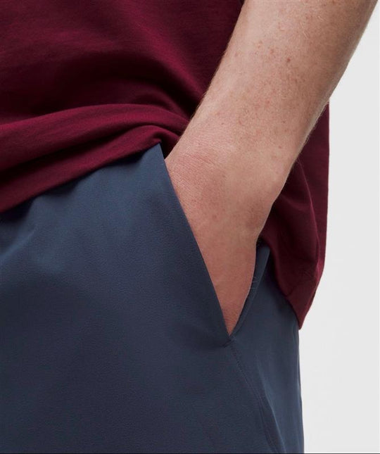 Close-up of a person wearing a dark navy blue pair of SHORTS and a burgundy top, with their hand tucked into the pocket of the shorts.