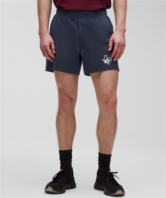 A model from the waist down wearing navy athletic shorts with a white Texas outline logo on the left leg, paired with a maroon shirt, black socks, and black sneakers against a light gray studio background.