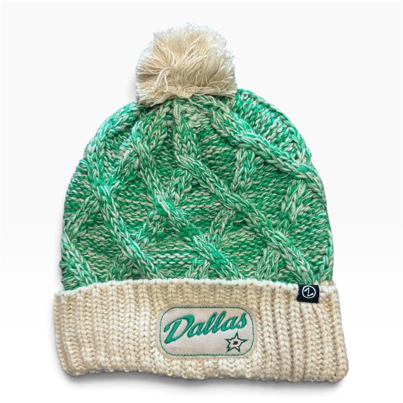 A green and cream cable-knit beanie hat with a cream pom-pom on top and a cream ribbed cuff. The cuff features a patch that reads &