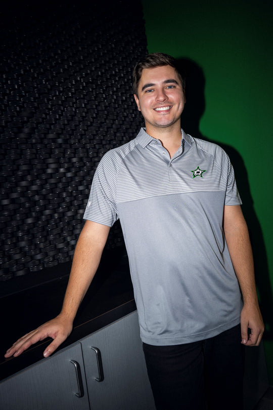 Man wearing a gray polo shirt with a Dallas Stars logo, standing against a dark background