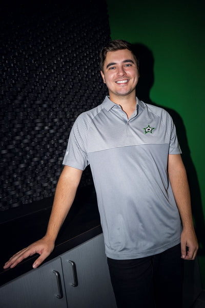 Man wearing a gray polo shirt with a Dallas Stars logo, standing against a dark background