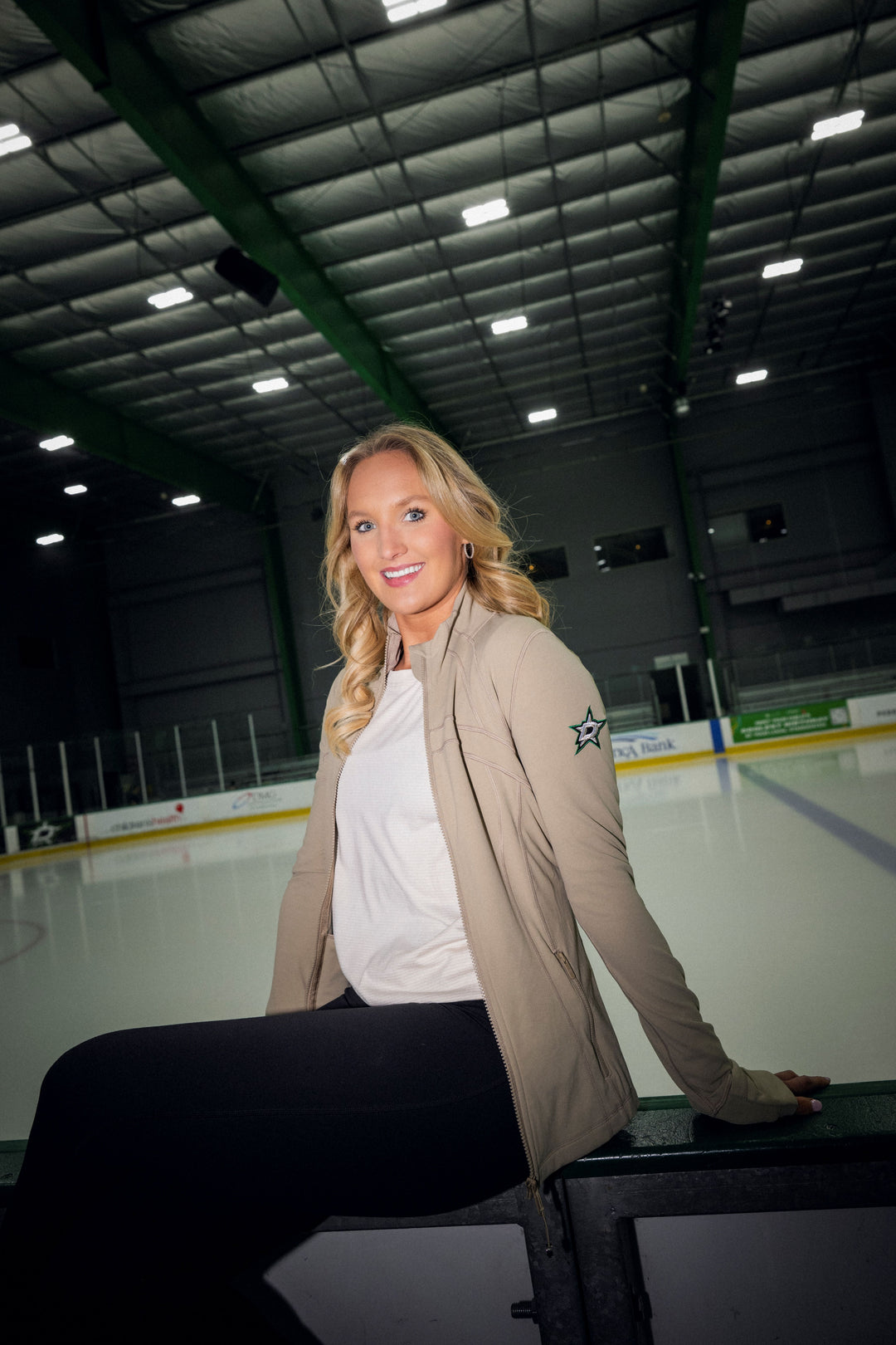 Woman posing on an ice rink wearing a beige jacket with a Dallas Stars logo.