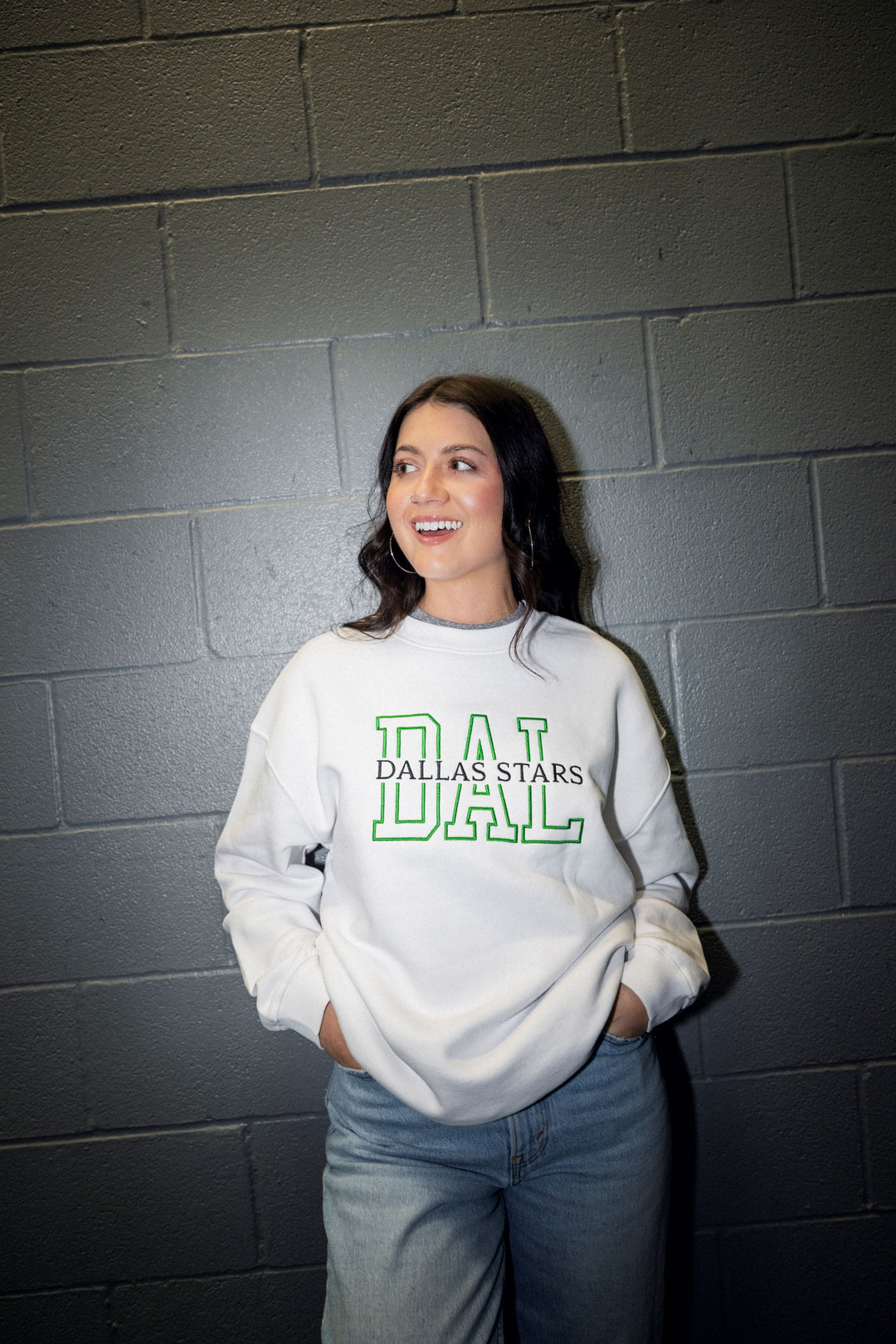 Person wearing a white sweatshirt with 'Dallas Stars' text against a gray brick wall