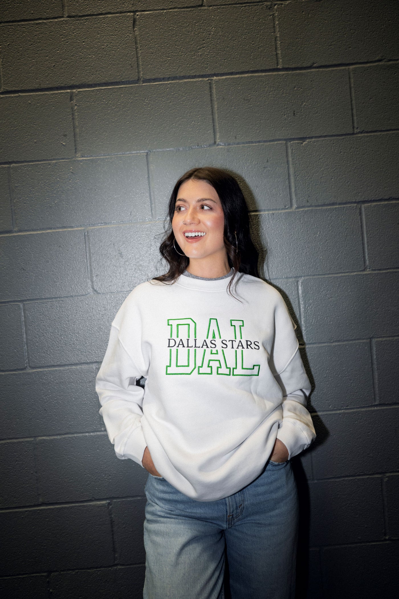 Person wearing a white sweatshirt with 'Dallas Stars' text against a gray brick wall